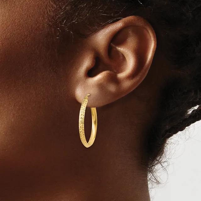 A close-up of a person's ear wearing a pair of textured gold hoop earrings with a hammered finish.