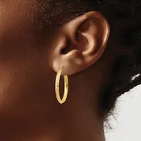A close-up of a person's ear wearing a pair of textured gold hoop earrings with a hammered finish.