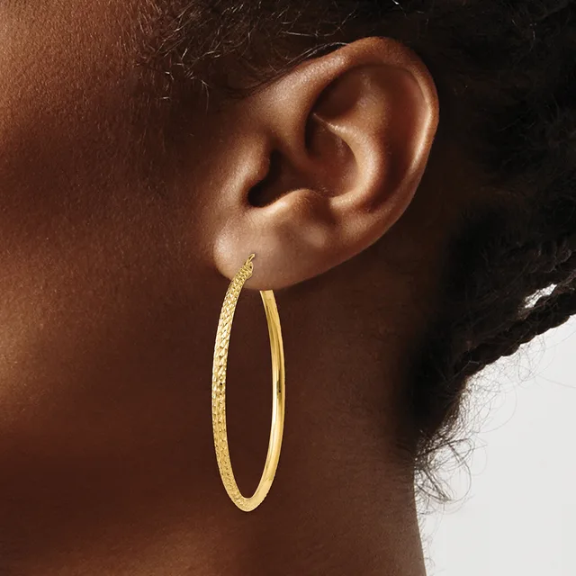 A woman wearing a pair of gold hoop earrings with a textured finish on one side and smooth on the other.
