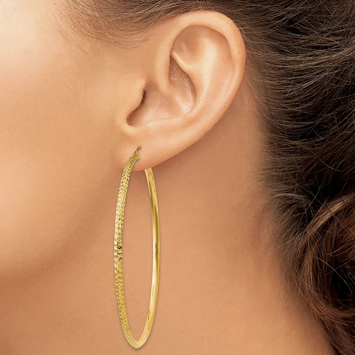 A woman wearing two gold hoop earrings of different textures—one with a hammered finish and one smooth—viewed from the side profile.
