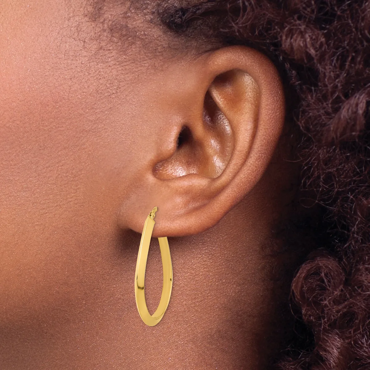 Gold hoop earrings with a matte finish worn on the earlobe of a person with medium brown skin tone and dark curly hair.