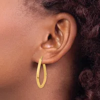 Gold hoop earrings with a matte finish worn on the earlobe of a person with medium brown skin tone and dark curly hair.