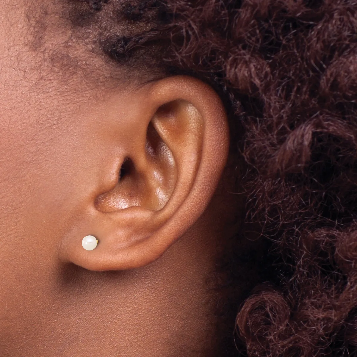 A close-up side view of a person's ear wearing a small white pearl stud earring in the lower lobe.