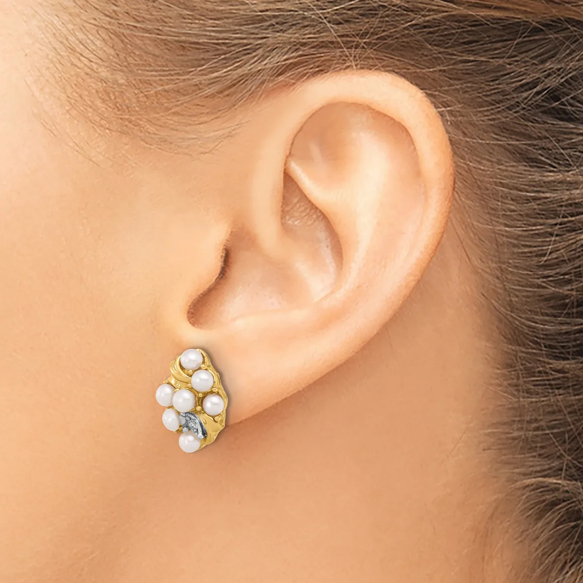 A gold-toned earring with multiple white pearl and crystal stones arranged in a clustered oval design, shown on a model's earlobe.