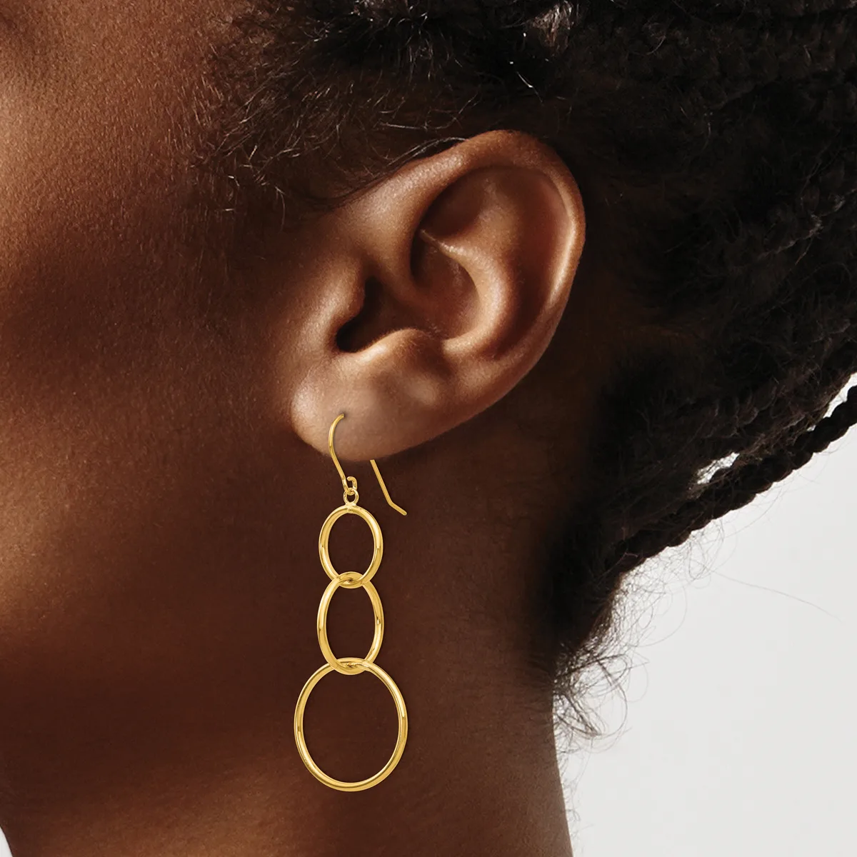 A person wearing a gold-colored dangle earring composed of three connected circular rings that decrease in size from top to bottom.