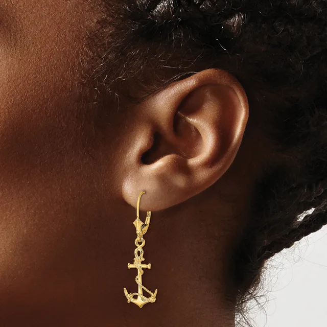 A gold anchor charm dangles from a gold hoop earring worn on a person's ear.