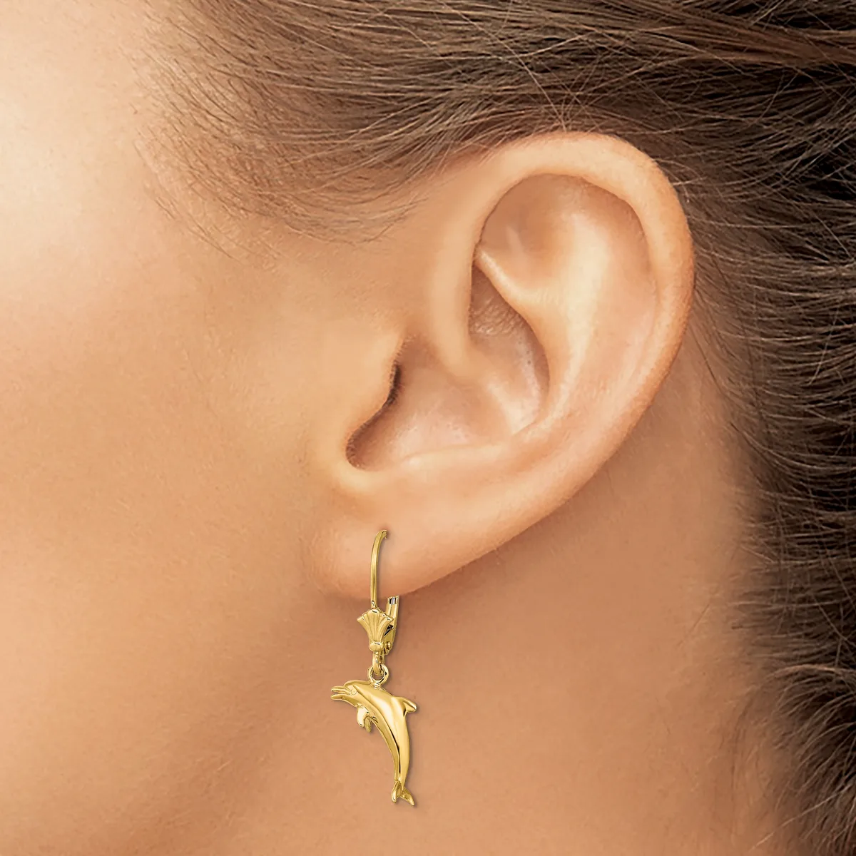 A person wearing a gold dolphin charm earring on a leverback hook, shown from the side view of their ear.