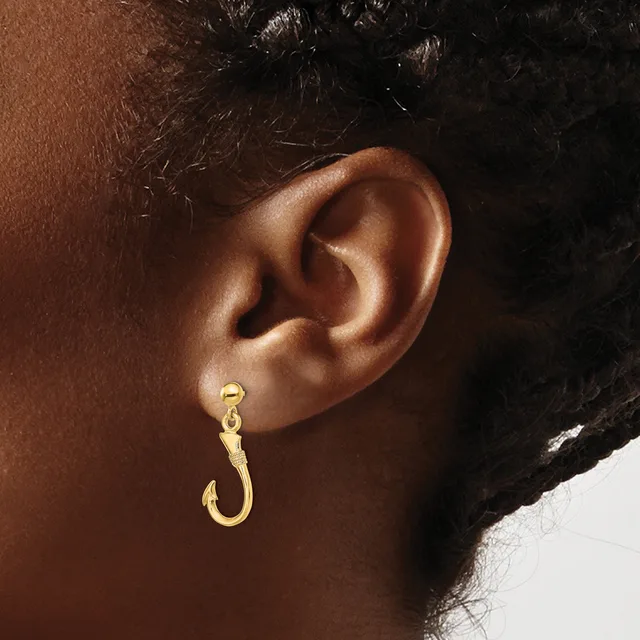 A person wearing a gold hook-shaped earring with a textured finish on their earlobe.