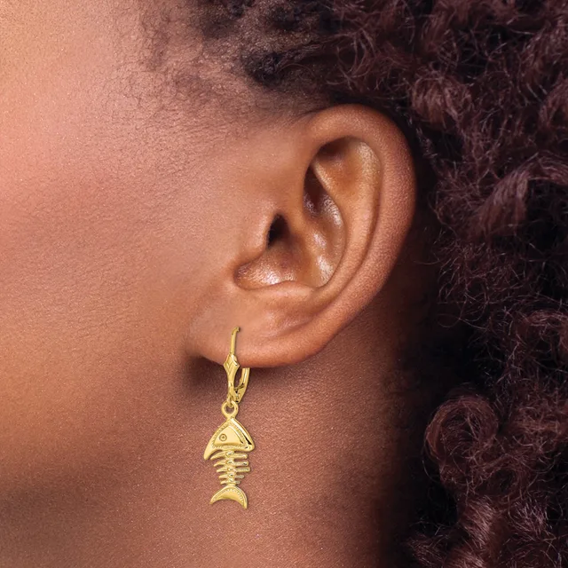A person wearing a gold fish skeleton charm earring hanging from a gold hoop on their earlobe.