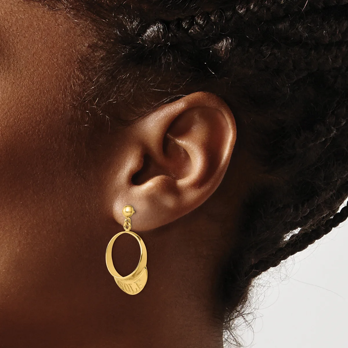 A person wearing a gold oval dangle earring with a textured finish, shown from the side view against their ear.