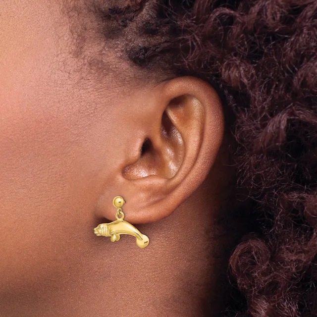A gold dangle earring shaped like a panther or leopard hangs from a ball stud on a person's earlobe.