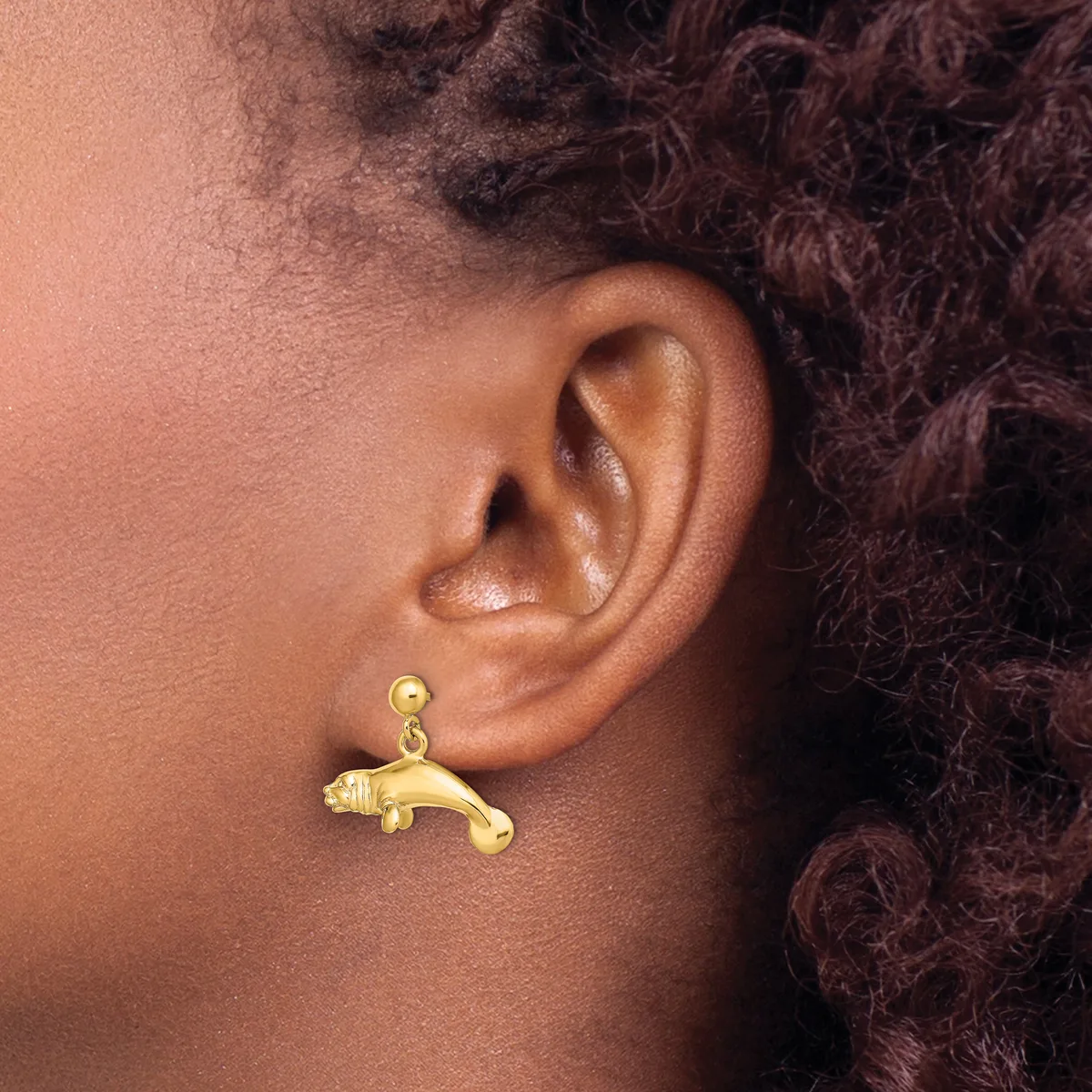 A gold dangle earring shaped like a panther or leopard hangs from a ball stud on a person's earlobe.