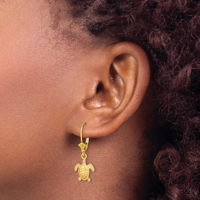 A gold turtle charm hangs from a gold hoop earring worn on a person's ear.