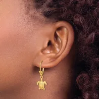 A gold turtle charm hangs from a gold hoop earring worn on a person's ear.