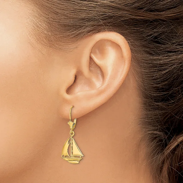 A woman wearing a gold sailboat charm earring on a lever-back hook, shown from the side view of her ear and neck.