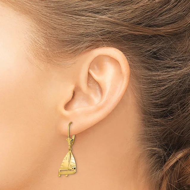 A woman wearing a gold sailboat-shaped dangle earring on a hook post, shown from the side view of her ear.