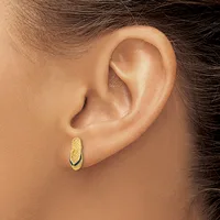 A person wearing a gold oval hoop earring with a textured surface, shown from the side view against their ear.