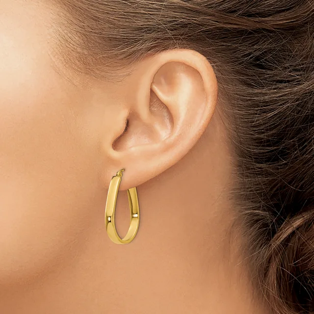 A person wearing a pair of gold-toned oval hoop earrings with a polished finish, shown from the side view against their ear.
