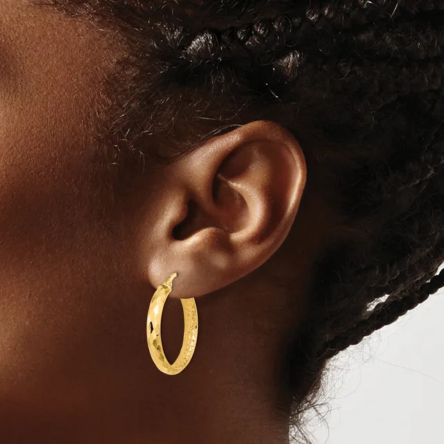 A person wearing a gold hoop earring with a textured surface, shown from the side view of their ear and neck.