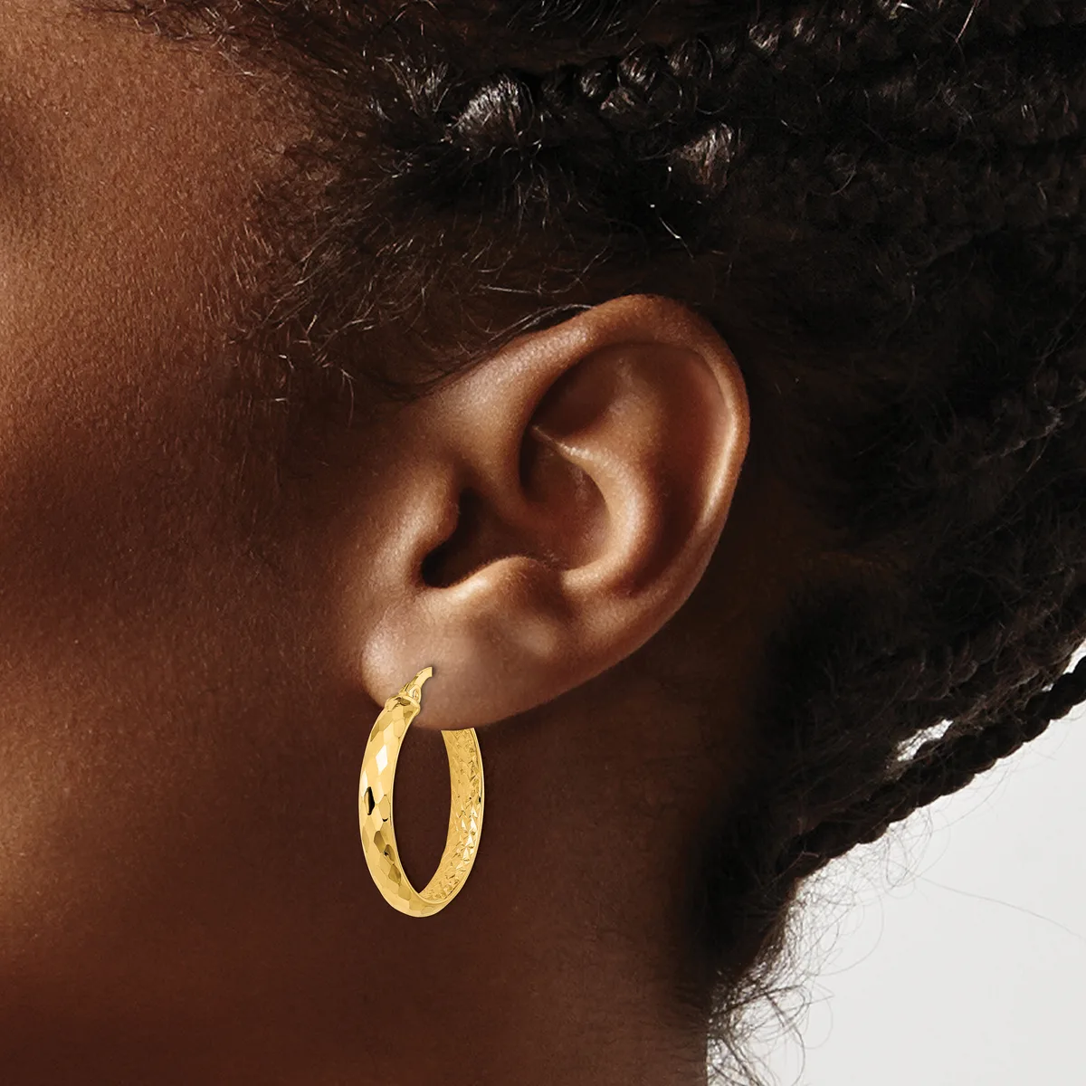 A person wearing a gold hoop earring with a textured surface, shown from the side view of their ear and neck.