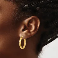 A person wearing a gold hoop earring with a textured surface, shown from the side view of their ear and neck.