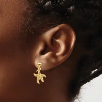 A gold starfish-shaped dangle earring worn on a person's earlobe, shown from the side view against their shoulder.