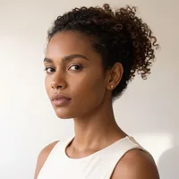 A woman with curly brown hair in an updo wearing a white sleeveless top, photographed in profile against a neutral background.