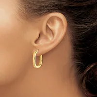 A person wearing a pair of polished gold hoop earrings, shown from the side profile of their ear and neck.