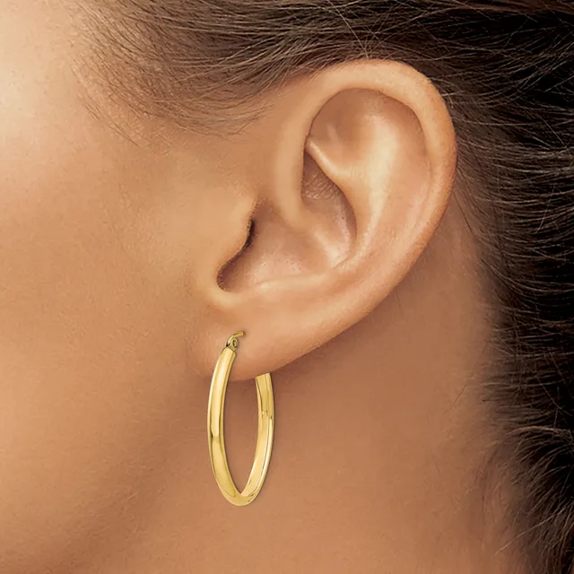 A person wearing a pair of polished gold hoop earrings, shown from the side profile of their ear and neck.