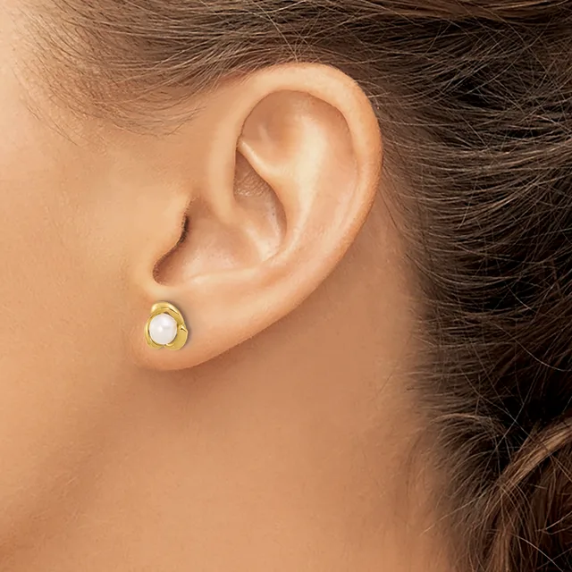 A person wearing a gold stud earring with a white oval stone or pearl set in the center, shown from a side profile view near the ear.