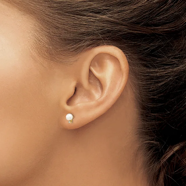 A close-up side view of a person's ear wearing a small white pearl stud earring with a metal backing.