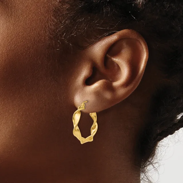 A person wearing a pair of twisted gold hoop earrings shown from the side profile of their ear.