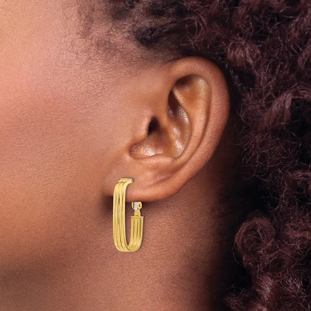 A person wearing a pair of polished gold-toned hoop earrings with a ribbed or textured surface, shown from the side profile against their ear.