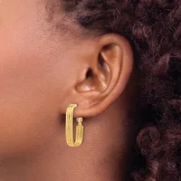 A person wearing a pair of polished gold-toned hoop earrings with a ribbed or textured surface, shown from the side profile against their ear.