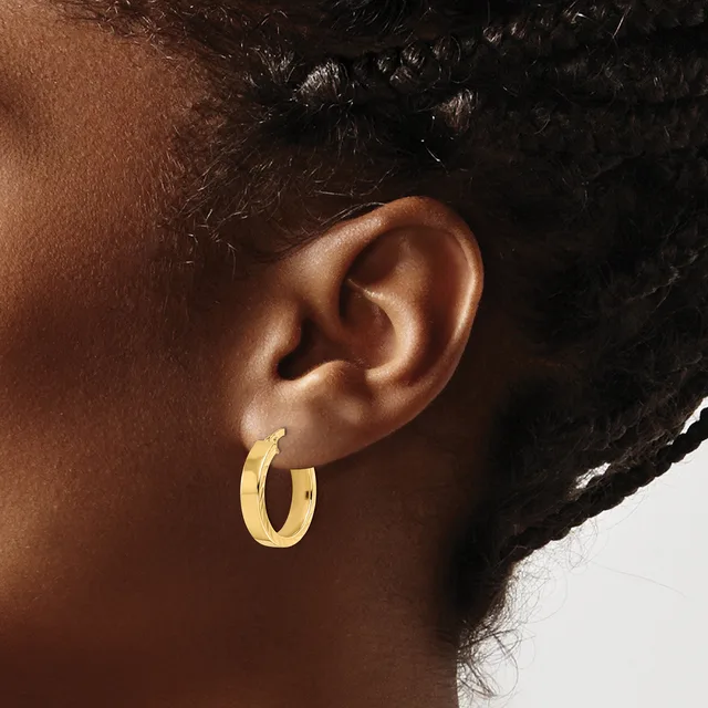 A person wearing a pair of polished gold hoop earrings, shown from the side profile of their head and ear.