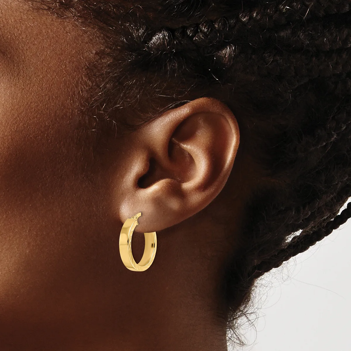 A person wearing a pair of polished gold hoop earrings, shown from the side profile of their head and ear.