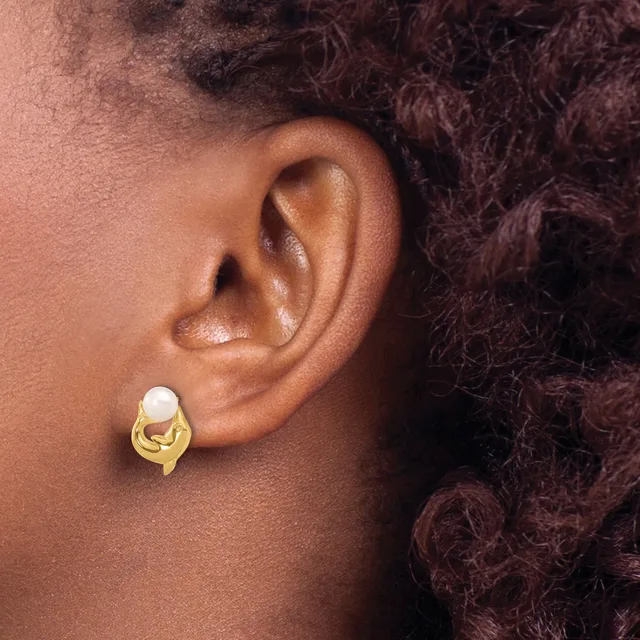 A close-up view of a person's ear wearing a gold-toned stud earring with a white pearl set in a curved, looped design.