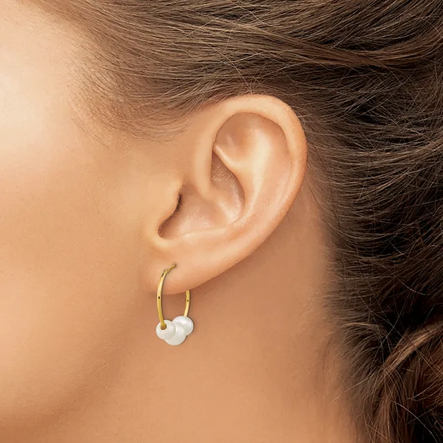 A person wearing gold hoop earrings with white pearl or bead charms hanging from them, shown from the side view of their ear.