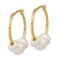A pair of gold hoop earrings with white pearl charms suspended from the bottom.