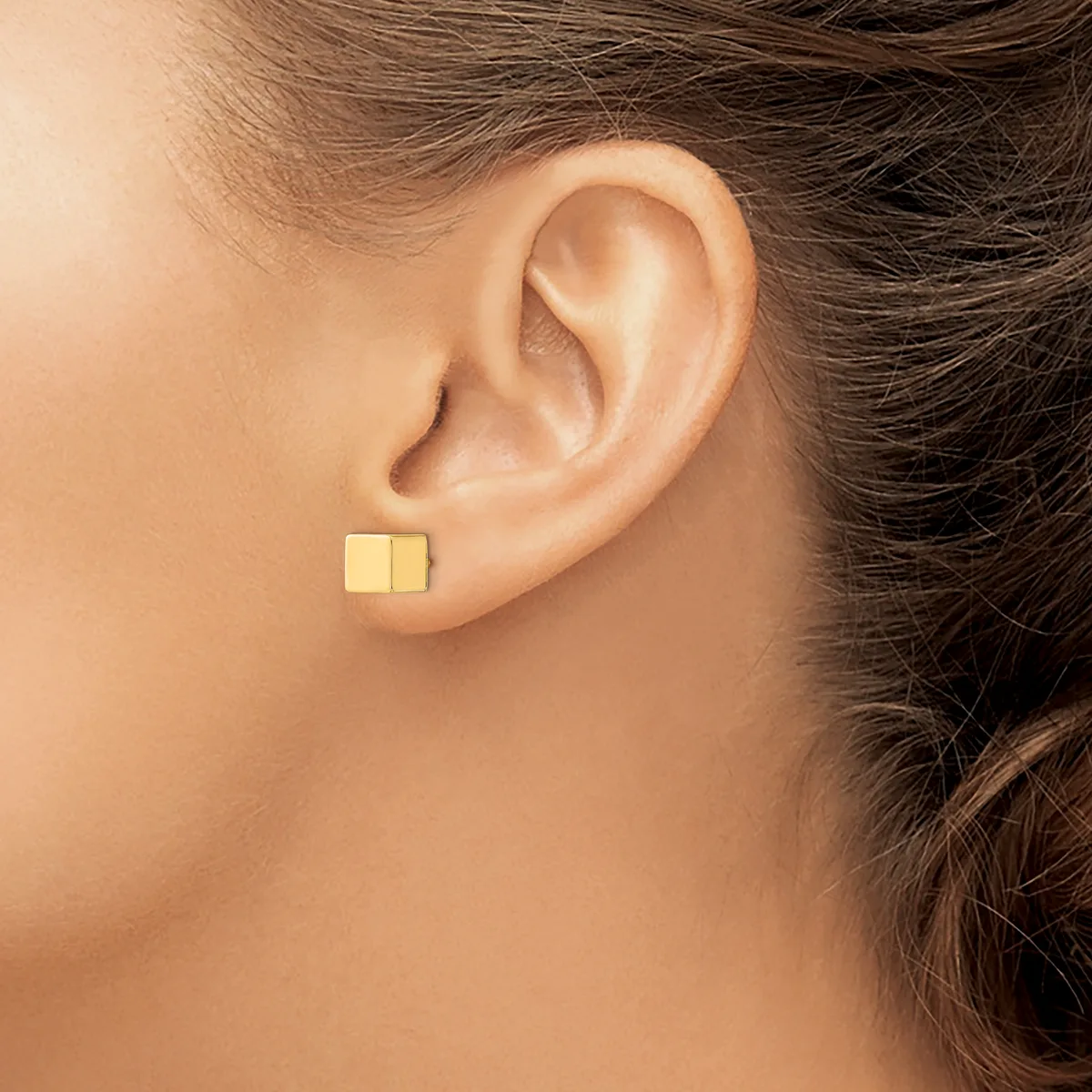 A person wearing small gold square stud earrings, shown from the side profile of their ear and neck.