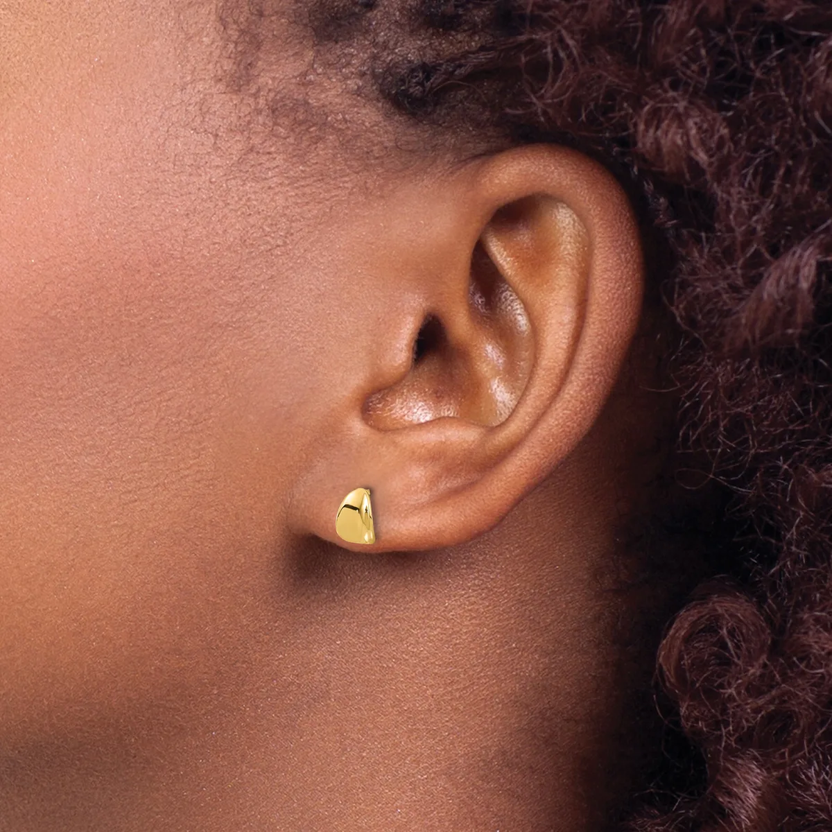 Side profile of a person wearing a small polished gold curved stud earring in their earlobe.