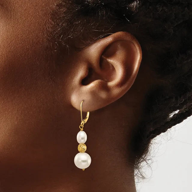 A person wearing a gold hoop earring with two stacked white pearl drops separated by a textured gold bead.