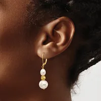 A person wearing a gold hoop earring with two stacked white pearl drops separated by a textured gold bead.