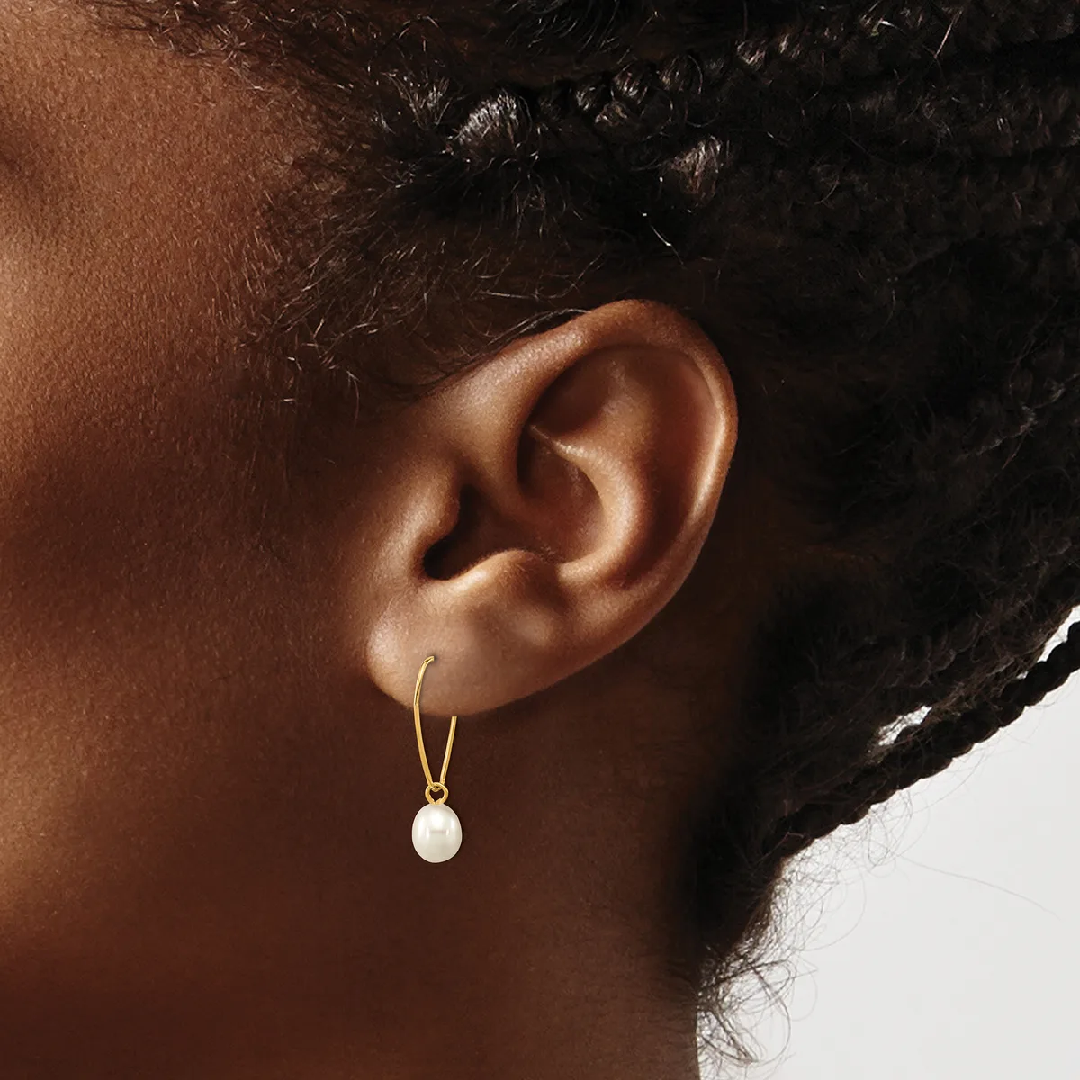A woman wears gold-toned hoop earrings with white pearl drops, shown from the side profile against a neutral background.