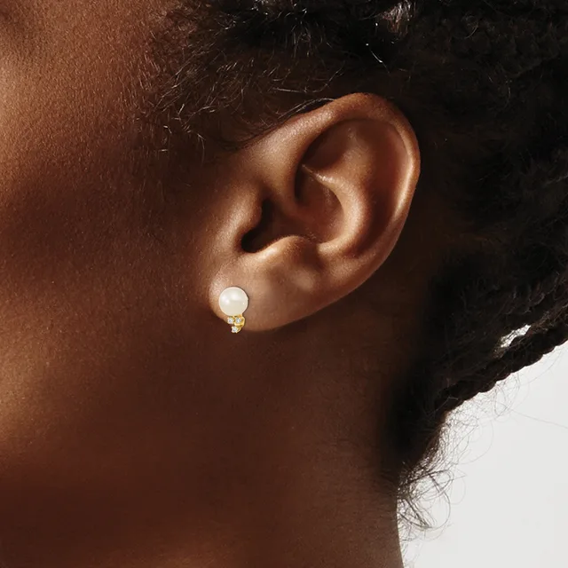 A person wearing a gold earring with a white pearl and small decorative element, shown from the side view of their ear and neck.