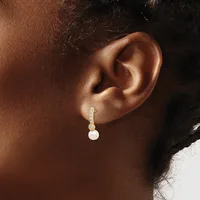 A person wearing a dangling earring with a pearl drop and diamond-studded curved connector on a post back, shown from the side view of their ear.