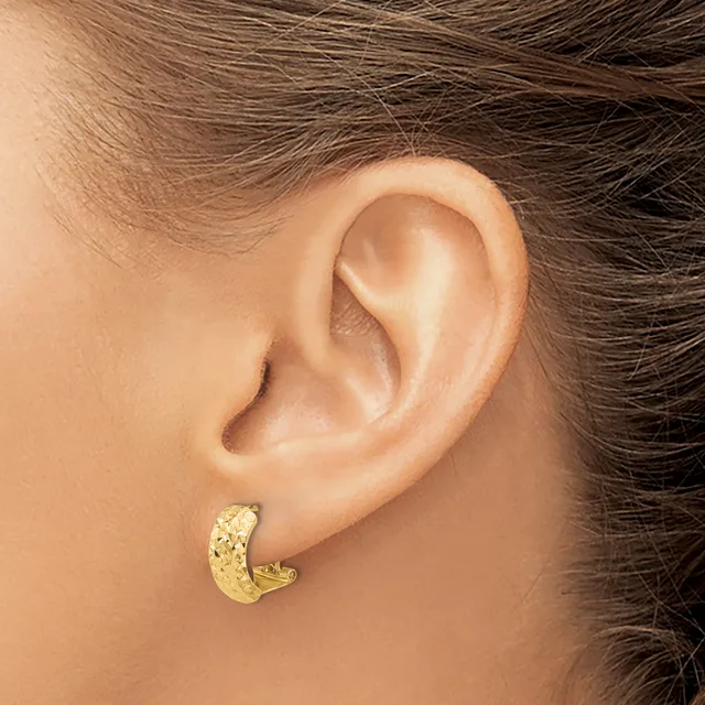 A textured gold hoop earring is worn on the earlobe of a person with brown hair.