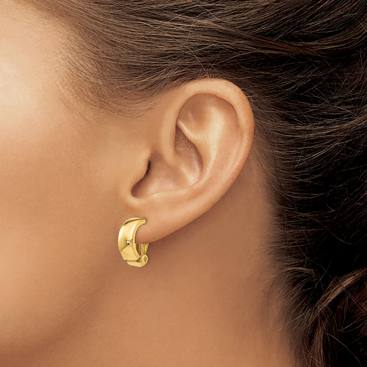 A person wearing a gold-colored chunky curved hoop earring in their pierced earlobe, shown in profile against their skin.