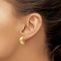 A person wearing a gold-colored chunky curved hoop earring in their pierced earlobe, shown in profile against their skin.