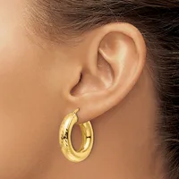 A person wearing a pair of polished gold hoop earrings with a twisted texture, shown from the side view against their ear.